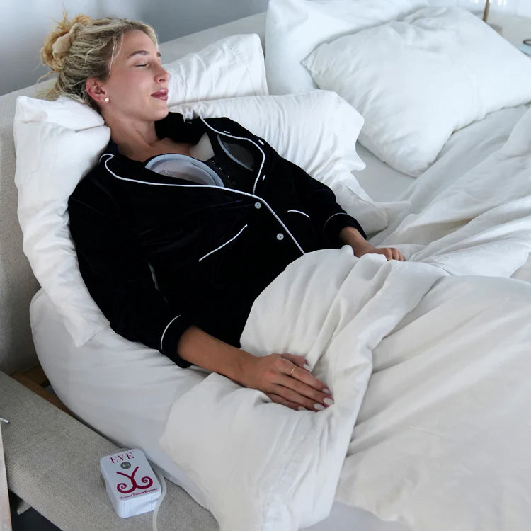 Woman wearing EVEBRA while resting in bed, with the EVE pump beside her